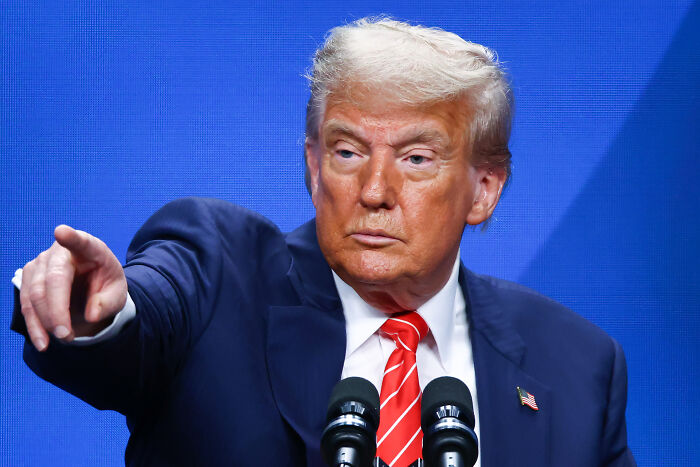 Man in a suit and red striped tie speaking at a podium, symbolizing health cuts impacting women&rsquo;s reproductive rights.