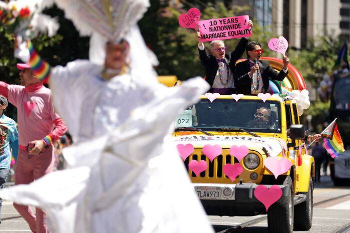 Participants celebrate marriage equality with pink heart signs and rainbow flags during a parade, highlighting same-sex marriage issues.
