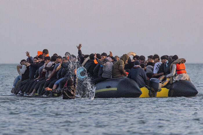 Overcrowded inflatable boat with migrants at sea, highlighting clashes involving French cops and UK-bound boarding attempts.