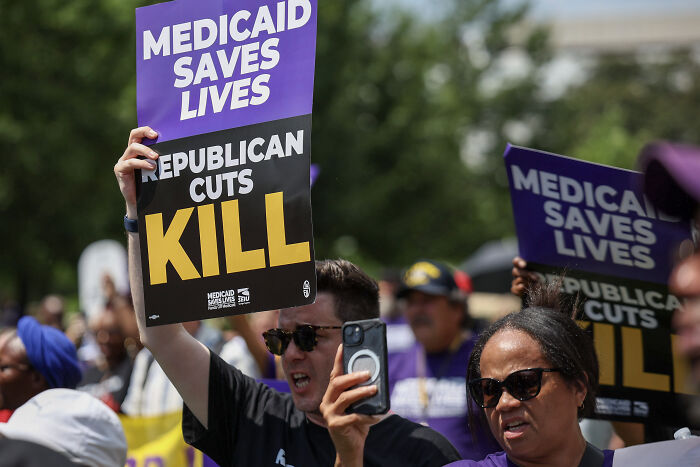 Protesters holding signs against health cuts, highlighting impact on Medicaid and women's reproductive rights in the U.S. and abroad.