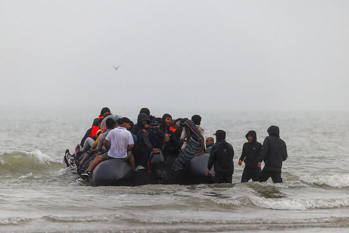 Group of people in life jackets and dark clothing boarding an inflatable boat amid tense French cops confrontation near shore.