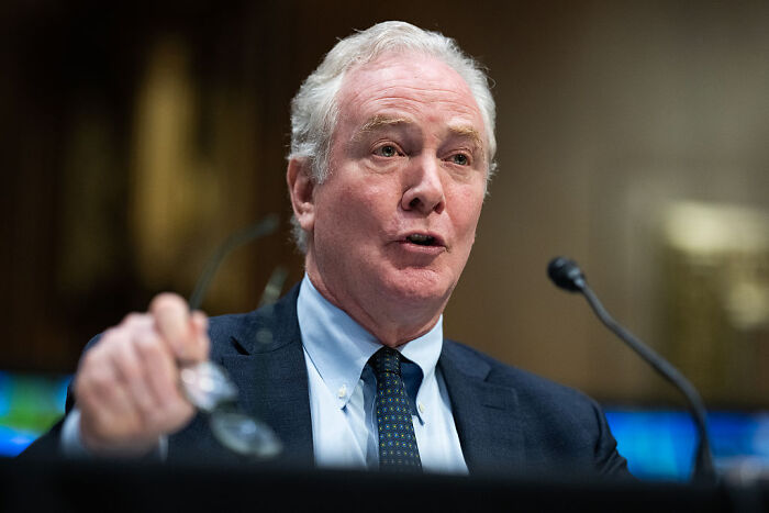 Man speaking at a hearing, raising glasses, illustrating question over FBI&rsquo;s legal right in Texas redistricting standoff.