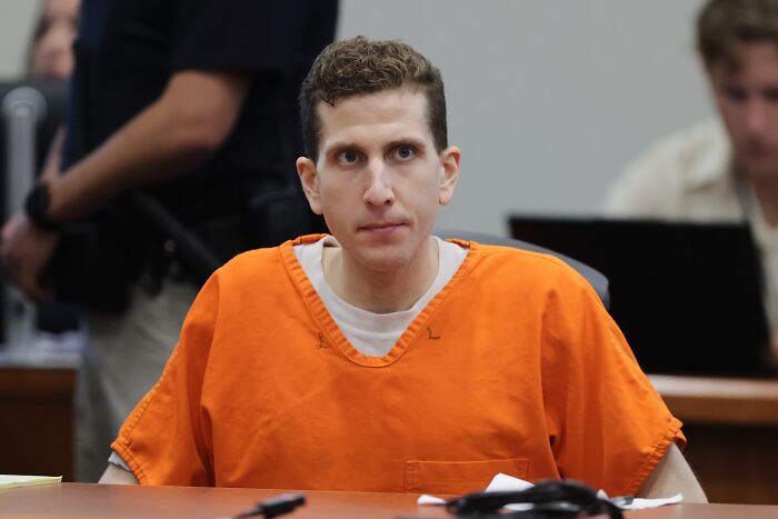 Man in an orange prison jumpsuit seated at a courtroom table during a legal proceeding involving prison harassment.