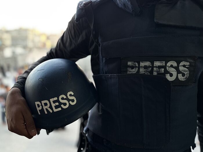 Journalist wearing black press vest and holding a press helmet, highlighting dangers faced amid low global press freedom.