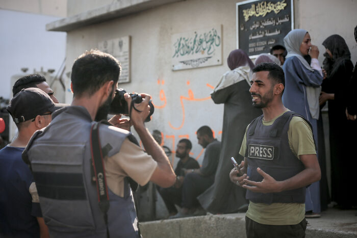 Journalists wearing press vests reporting and taking photos amid concerns over press freedom and journalist safety in conflict areas.