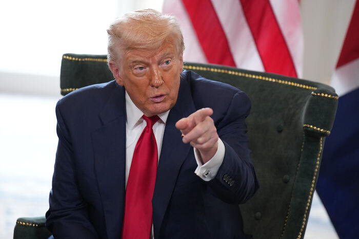 Former President Trump in a navy suit and red tie pointing while seated during an interview discussing Trump Charlamagne Tha God.