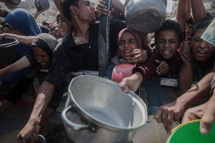 Crowd of desperate people in Gaza reaching out with empty pots amid war and hostage crisis tensions.