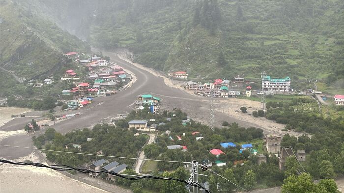 A town surrounded by severe flash floods with muddy water sweeping through streets and buildings in a mountainous area.