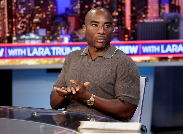 Charlamagne Tha God seated in a studio discussing topics, wearing a brown shirt and a gold watch.
