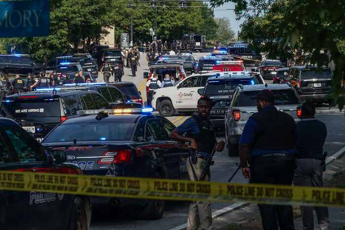 Police officers gathered behind yellow tape with multiple vehicles blocking a street amid CDC leaders resigning warnings over RFK Jr. health plans