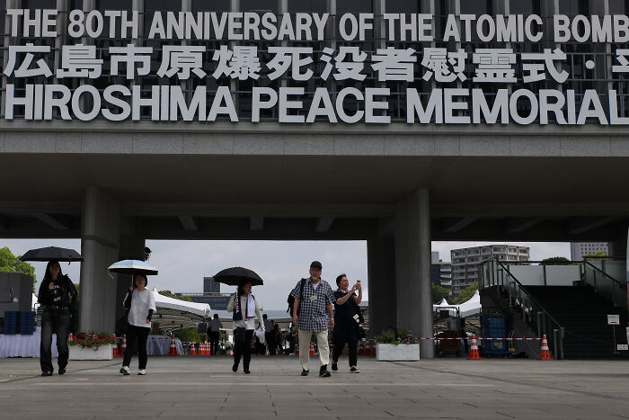 Visitors walk under Hiroshima Peace Memorial signage, reflecting on the 80-year aftermath of Hiroshima and Nagasaki to avoid World War III.