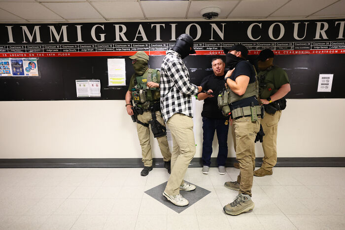 Masked officers in tactical gear detain a man inside an immigration court hallway related to ICE enforcement actions.