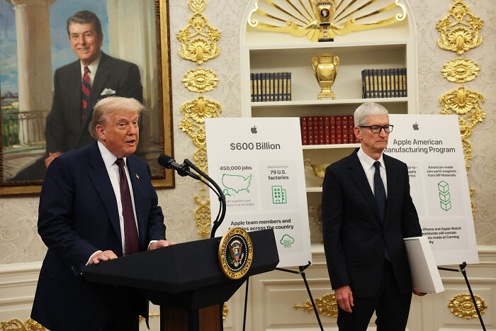 Tim Cook holding a gold Apple gift next to Donald Trump speaking at a White House event with gold decor.