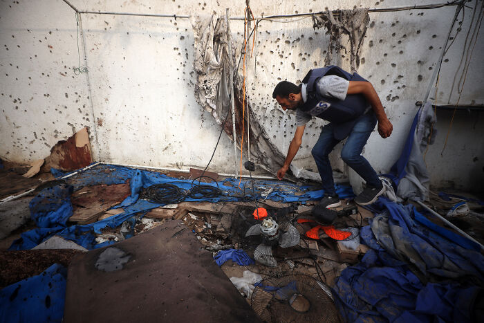 A man wearing protective gear inspects debris in a damaged building amid declining global press freedom and journalist deaths.