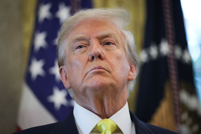 Close-up of Donald Trump standing serious with U.S. flag behind, related to West Bank-style occupation of Ukraine talks.