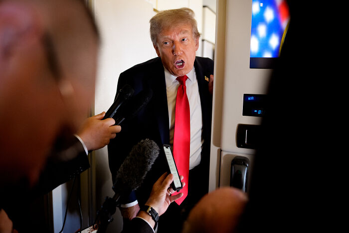 Donald Trump speaking passionately to reporters with microphones pointed toward him during a media interaction.