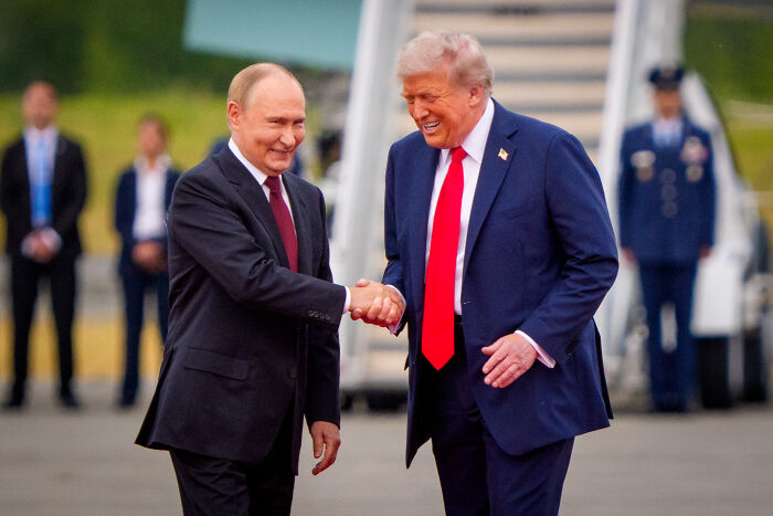 Donald Trump shaking hands with Vladimir Putin outdoors, discussing Ukraine war and Zelenskyy actions.