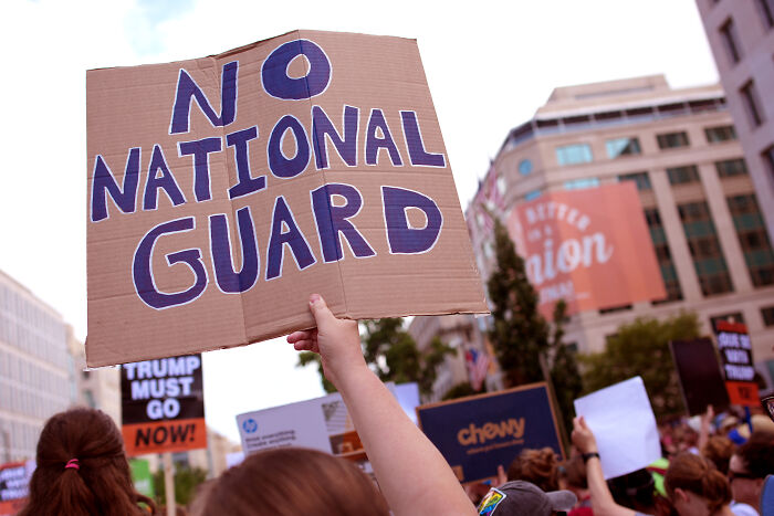 Protesters in Washington, D.C. hold signs including one saying no National Guard during Trump's federal takeover debate.