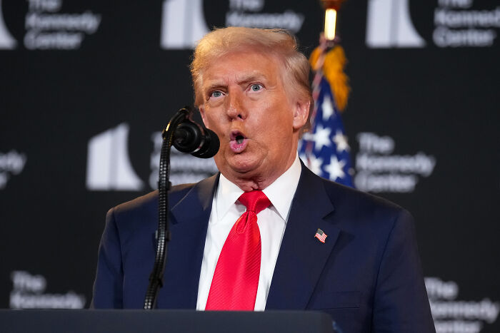 Donald Trump speaking passionately at a podium with microphone and American flag in background during event.