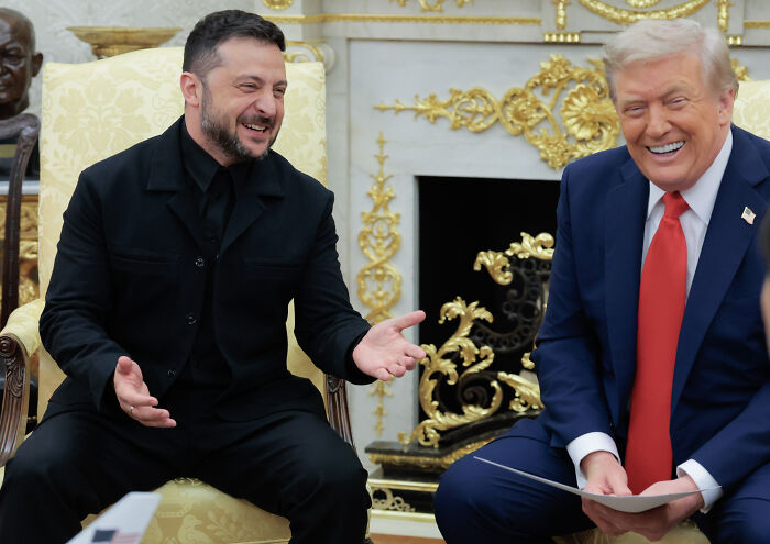 Volodymyr Zelenskyy wearing a black suit during a White House meeting with Donald Trump, both smiling and engaged.