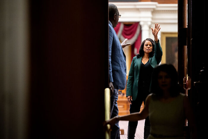 Woman raising her hand inside a government building during a Texas GOP session on a controversial partisan redistricting map.
