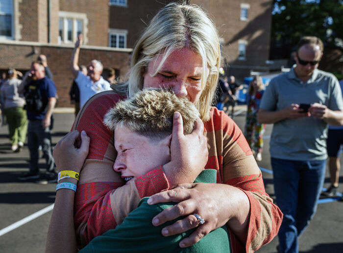 A distressed 5th grader being comforted by an adult outside a school after the Minneapolis school tragedy incident.