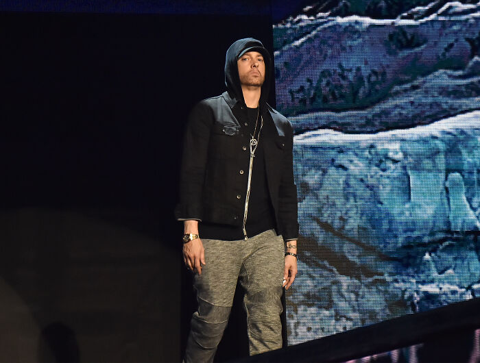 Eminem in a black hoodie and gray pants on stage, linked to early views on MAGA going viral online.