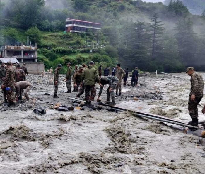 Rescue team navigating severe flash floods in a town with turbulent waters and damaged structures among mountainous terrain.