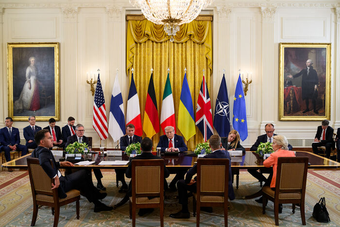 Leaders in a formal White House meeting room with national flags, Zelenskyy and others discussing important diplomatic matters.
