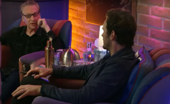 Chris Pratt seated and talking with another man in a cozy room, referring to his wife's relative RFK Jr. amid MAHA uproar.