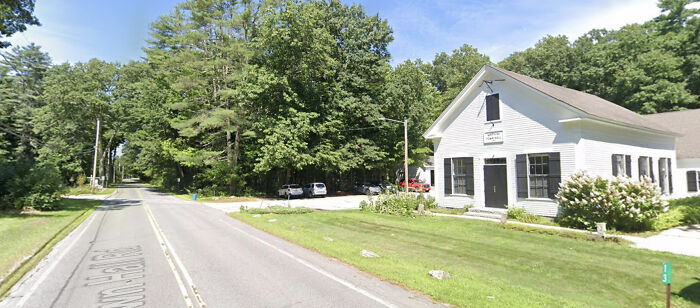 Rural street with trees and a white building, illustrating a quiet setting linked to brain cancer and family tragedy.
