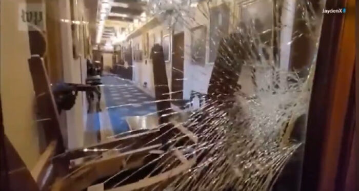 Shattered glass door with people in the hallway, related to Jan 6 Capitol rioter receiving full military funeral honors.