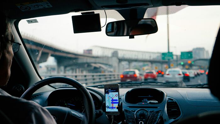 View from inside a car showing Uber driver using navigation app amid alleged driver screening failures causing lawsuits across US.