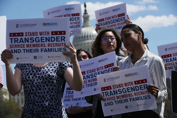 Protesters holding signs supporting transgender service members and retirement pay rights near U.S. Capitol building.