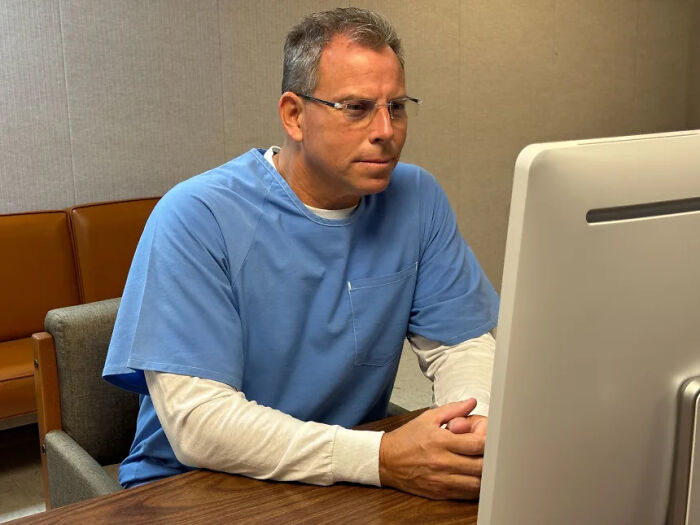 Man in prison uniform sitting at a desk looking at a computer screen, related to Erik Menendez denied parole news.