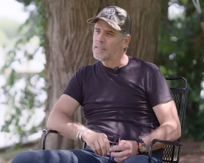 Man in a black shirt and camo hat sitting outdoors near a tree, discussing Prince Andrew book and Jeffrey Epstein claims.
