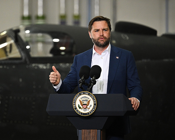 D Vance speaking at podium with presidential seal, sparking villagers&rsquo; fury over disabled parking convoy incident.