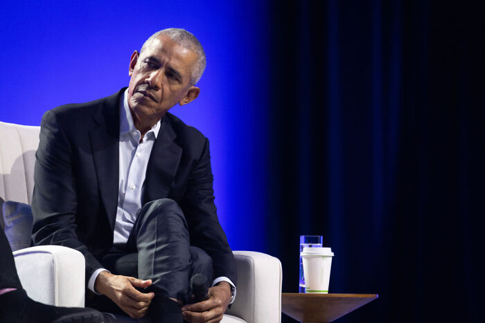 Barack Obama seated on stage in a dark suit, speaking on redistricting and Texas GOP partisan map in a public event.