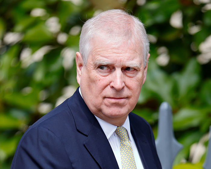 Prince Andrew outdoors in a suit and yellow tie, looking sideways amid green foliage, related to Jeffrey Epstein claims.