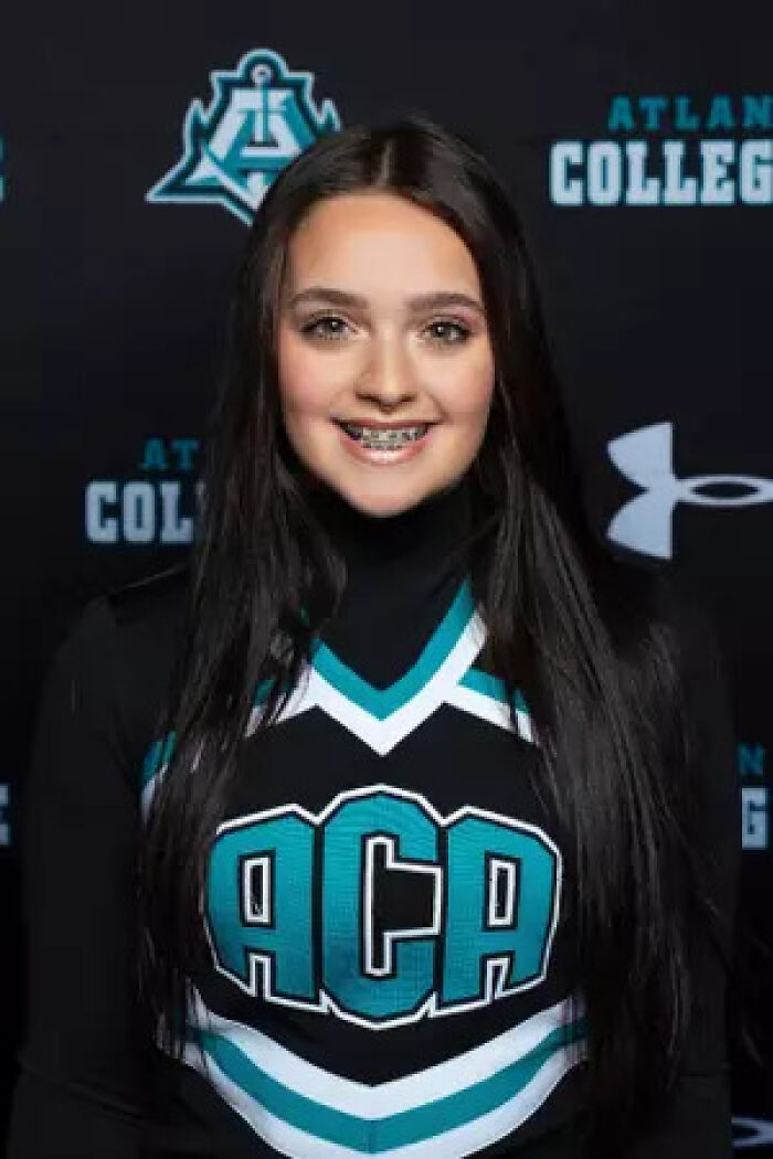 Teen girl cheerleader in ACA uniform smiling at photo shoot with college logos in background, linked to slain teen case.