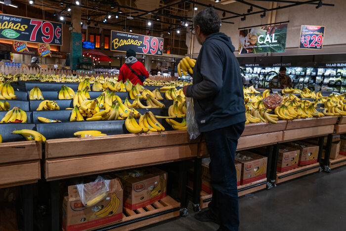 Man shopping for bananas in a grocery store highlighting Americans battling to afford essentials and rising food prices.