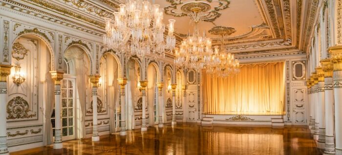 Luxurious White House ballroom with ornate chandeliers, intricate ceiling designs, and polished wooden floors.