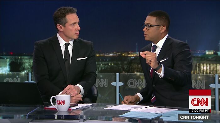 Two men in suits having a serious discussion on CNN Tonight, with city lights visible through the window behind them.