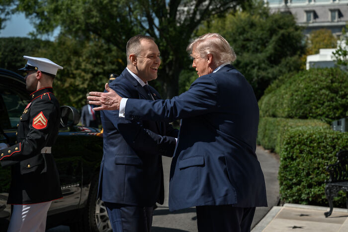Two men in suits greeting each other outdoors with a uniformed Marine nearby, symbolizing Poland defending its territory from Russian drones.