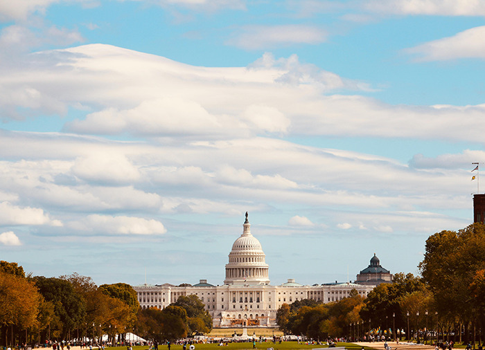 Wide view of the US Capitol with trees and people under a cloudy sky representing Brics dollar influence on global order.