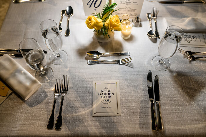 Table setting with water glasses, silverware, yellow roses, and a Rose Garden Club card at an event.