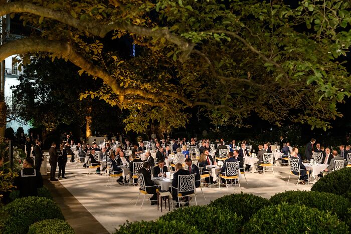 Outdoor formal dinner with guests seated at tables under trees, illustrating Newsom slams Trump&rsquo;s Rose Garden Club event.