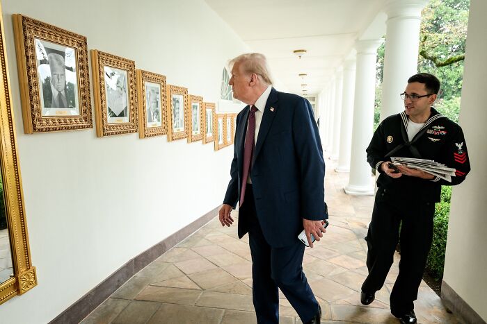 Former president examining framed portraits in the White House Presidential Walk of Fame hallway.