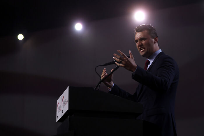 Man speaking passionately at a podium under bright lights, related to Charlie Kirk shooting conspiracy theories online.