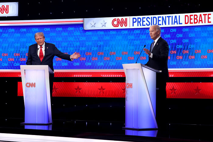 Two politicians onstage at CNN presidential debate with blue and red backdrop and podiums under bright studio lights